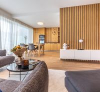 Living room in a family house with wood-patterned flooring and a dining area in the background.