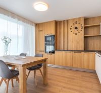 A kitchen with wooden decor, a dining table, gray chairs, and large windows.