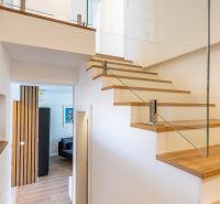 Interior of a family house with wooden stairs, glass railing, and flooring with a wooden decor.