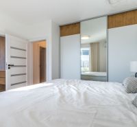 A bedroom in a family house with a large built-in wardrobe and a bed in light colors.
