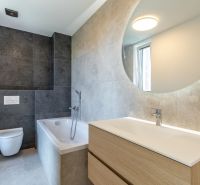 A bathroom in a family house with a bathtub, a sink, and tiles in dark tones.