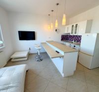 A kitchen in a studio apartment with bar stools and purple wall tiles.