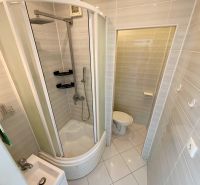 Bathroom with shower and toilet in a studio apartment, light tiles.