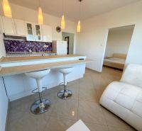 A kitchen with a bar counter in a studio apartment, white furniture, purple tiles, and an armchair.