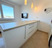 A kitchen in a studio apartment with a washing machine, white cabinets, and a countertop.