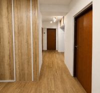 A hallway in a 3-room apartment with a wood-patterned floor and built-in wardrobes.