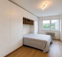 A bedroom in a three-room apartment with a bed, built-in wardrobes, and flooring with a wood decor.