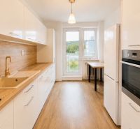 A kitchen in a 3-room apartment with a wooden decor floor, white cabinets, and a stove.