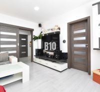 Living room in a three-room apartment with a wooden decor floor and white furniture.