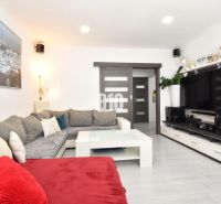 Living room in a three-room apartment with a corner sofa, television, and wooden decor flooring.