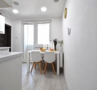 Dining area with a table and chairs on a floor with a wooden decor in a 3-room apartment.