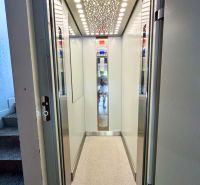 An elevator with an illuminated ceiling and light walls in a residential building.