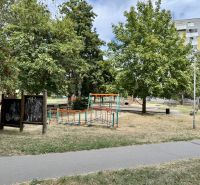 A children's playground surrounded by trees in a park in the town of Topoľčany near a one-bedroom apartment.