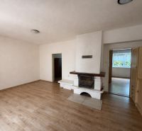 Interior of a family house with a fireplace, wood-patterned flooring, and simple furnishings.