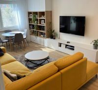 Living room in a 3-room apartment with a comfortable sofa, dining table, and wooden decor flooring.