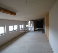 A narrow interior of a warehouse with white walls and a row of windows on the left side.