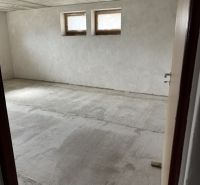 Unfurnished room in a family house with two small windows and a raw floor.