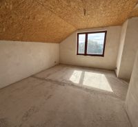 The interior of a family house with a window, slanted ceiling, and unfinished floor.