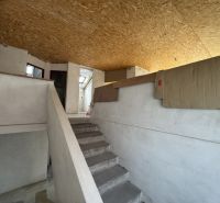 Interior of a family house with a staircase, white walls, and OSB boards on the ceiling.