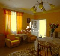 A living room in a family house with orange curtains and a table with a tablecloth.