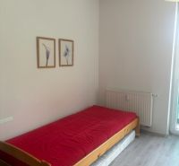 Studio apartment with a bed, red blanket, and wooden decor flooring.
