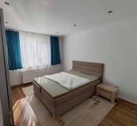 A bright bedroom in a three-room apartment with a wood-patterned floor and blue curtains.