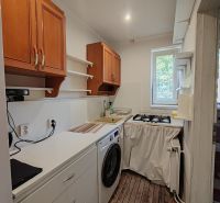 A kitchen in a 3-room apartment with wood-patterned flooring, a washing machine, and upper cabinets.