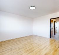 A room with a wooden decor floor in a 3-room apartment, white walls, open doors.