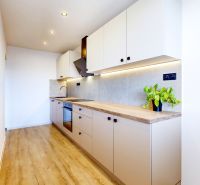 A kitchen in a 3-room apartment with a kitchen unit, flooring with a wood decor, and lighting.