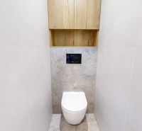 A bathroom with white tiled walls in a 3-room apartment, with a cabinet above the toilet.