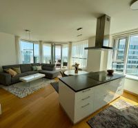 A bright living room with wood-patterned flooring in a three-room apartment, with a view from spacious windows.