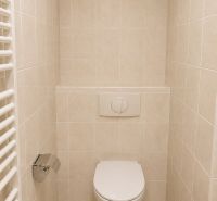 Bathroom toilet in a 2-room apartment with tiles and a wall-mounted flushing system.