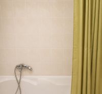 Bathroom with a bathtub, shower curtain, and light tiles in a 2-room apartment.
