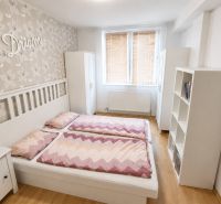 A bright bedroom with a double bed, floral wallpaper, and a wood-patterned floor.