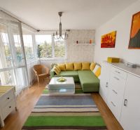 Living room with a corner sofa, wooden decor flooring, and a colorful carpet.