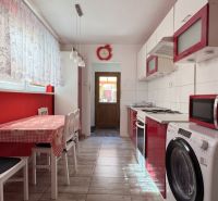A kitchen in a family house with a table, chairs, appliances, and red details.