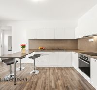 A kitchen with white cabinets, a colorful table, and a wood-patterned floor in a three-room apartment.