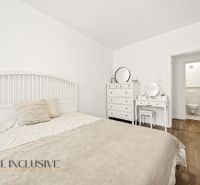 A bedroom in a three-room apartment with a bed, a dresser, and a floor with a wood decor.