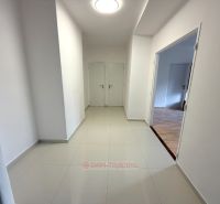 A corridor with light walls and tiles, entrance to a room with wood-patterned flooring.