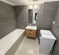 A bathroom with a bathtub, sink, washing machine, and gray walls in a 2-room apartment.