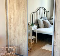 A mirrored wardrobe in a 2-room apartment with a wooden decor floor and a black bed.