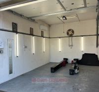 An empty garage with lighting, a garage door, a clock, equipment on the floor of the garden.