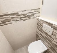 A toilet in a 2-room apartment with light tiles and practical storage space.