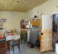 A kitchen in a family house with old equipment, a dining table, and patterned carpets.