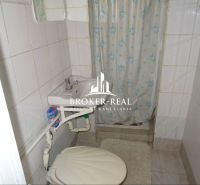 A bathroom in a family house with white tiles, a shower, and a sink.