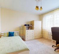 A bright room with a bed, a desk, a wooden floor, and curtains in a family house.