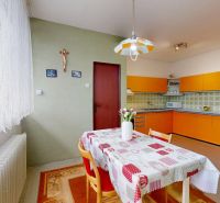 A kitchen in a family house with an orange kitchen unit, curtains, and floral decorations.