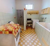 Bathroom in a family house with a bathtub, shower, and washing machine. Tiled floor.