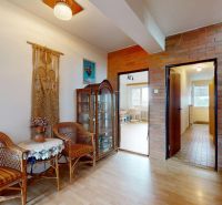 Interior of a family house with wicker chairs, a glass cabinet, and a wooden-patterned floor.
