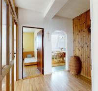 A hallway in a family house with a wooden decor floor, entrance to a room and kitchen.